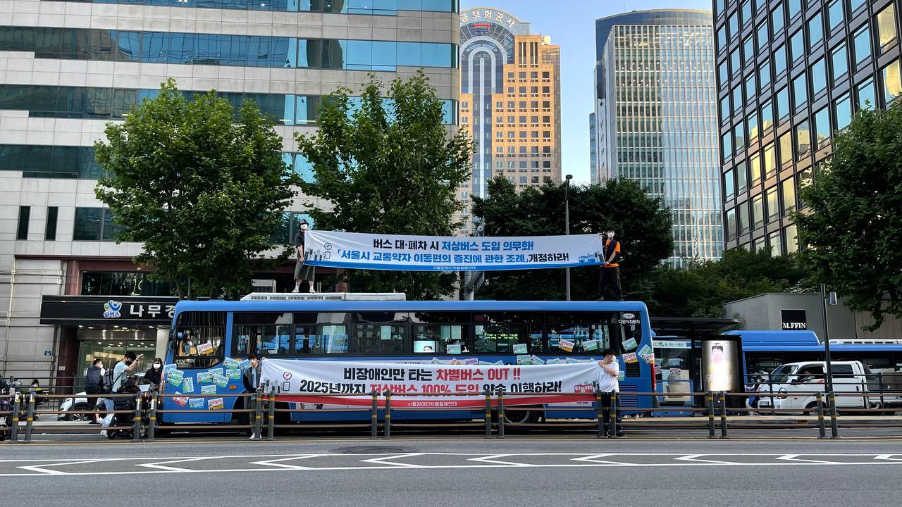 이동권_2021년 종로1가 버스정류장. 활동가들이 버스의 이동을 막고 버스 위에 올라가거나 버스 옆에 서서 \'비장애인만 타는 차별버스 OUT\' 현수막을 들고 있다..JPG