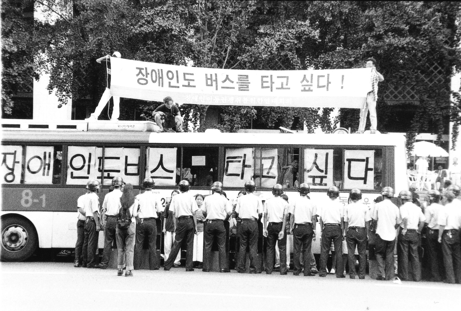 2001년 8월 29일 서울 광화문 세종문화회관 앞. 네 시간의 버스 점거 투쟁. 활동가들이 버스 위에 올라가 _장애인도 버스를 타고 싶다_ 라고 적힌 현수막을 들고 있다. 버스 창문에도 버스 타고 싶다는 글자가 한 글자씩 붙어있다. photo by 최병선.jpg